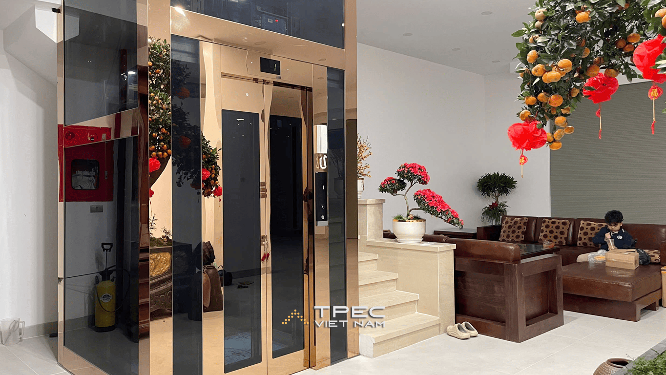 Thang máy kính khung inox gương đồng đặt tại sảnh tầng 1 nhà phố Trần Quang Diệu