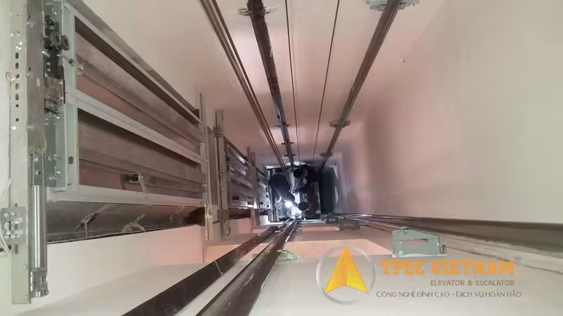 Hố thang máy nhìn từ dưới lên với hệ ray dẫn hướng và cáp tải khi chạy thử