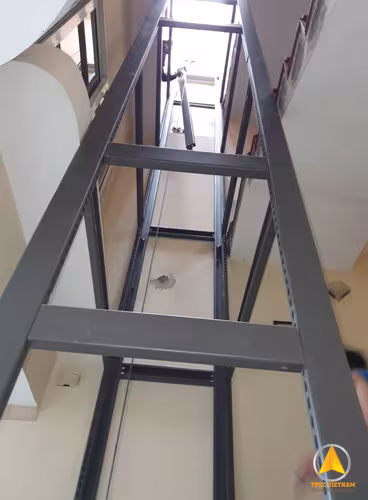 Khung thép thang máy sơn đen lắp bên trong nhà, nhìn từ dưới lên giếng thang
