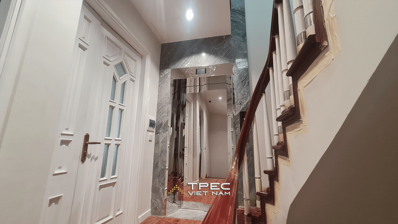Thang máy gia đình cửa inox gương ốp đá marble xám bên cầu thang nhà Nguyễn Khang