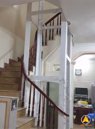 Thi công lắp dựng khung nhôm thang máy màu trắng bọc nilon bao quanh cầu thang gỗ trong nhà