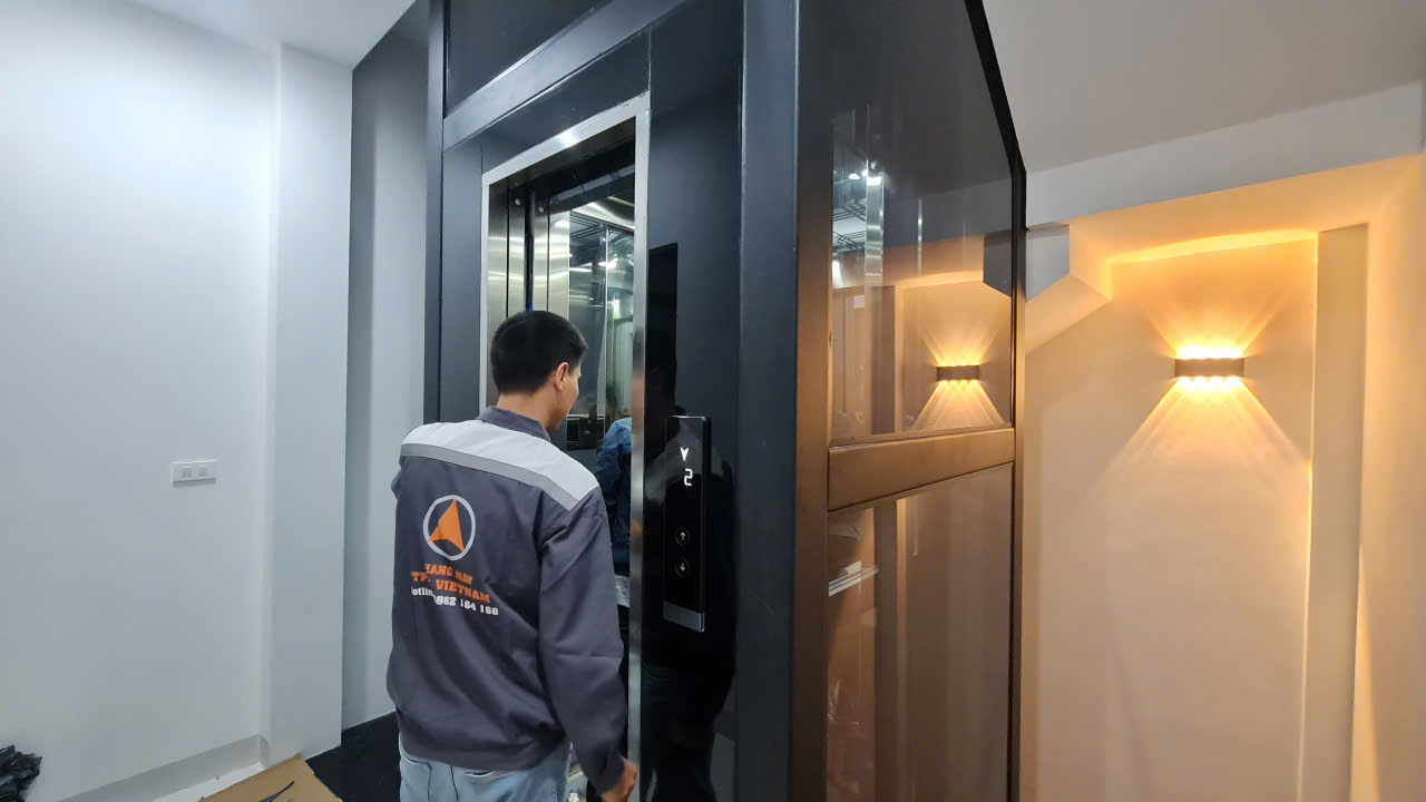 Kỹ thuật viên Thiên Thành Phát mở cửa cabin thang máy kính cạnh vách đèn trang trí, nhà phố Hà Đông