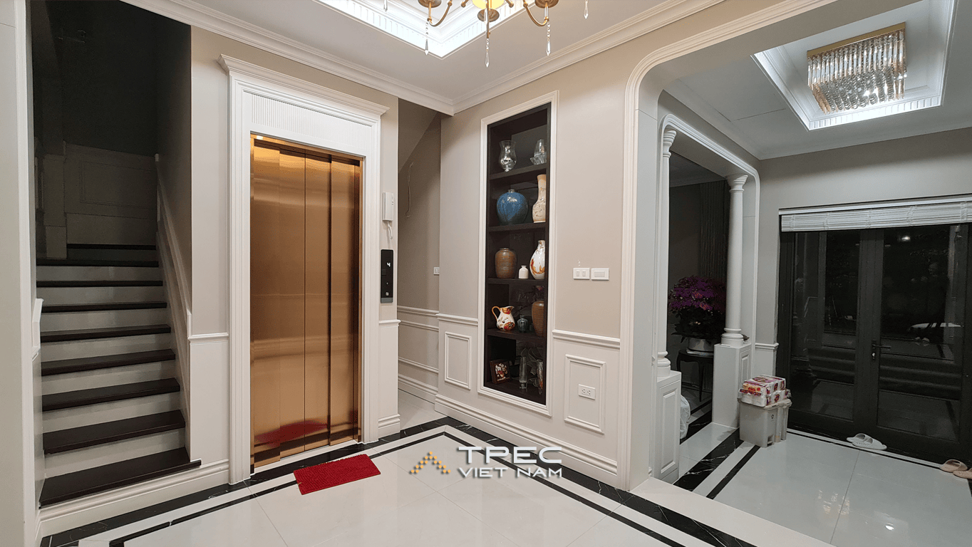 Thang máy cửa inox vàng cạnh cầu thang và kệ trang trí, sảnh biệt thự Xanh Villas