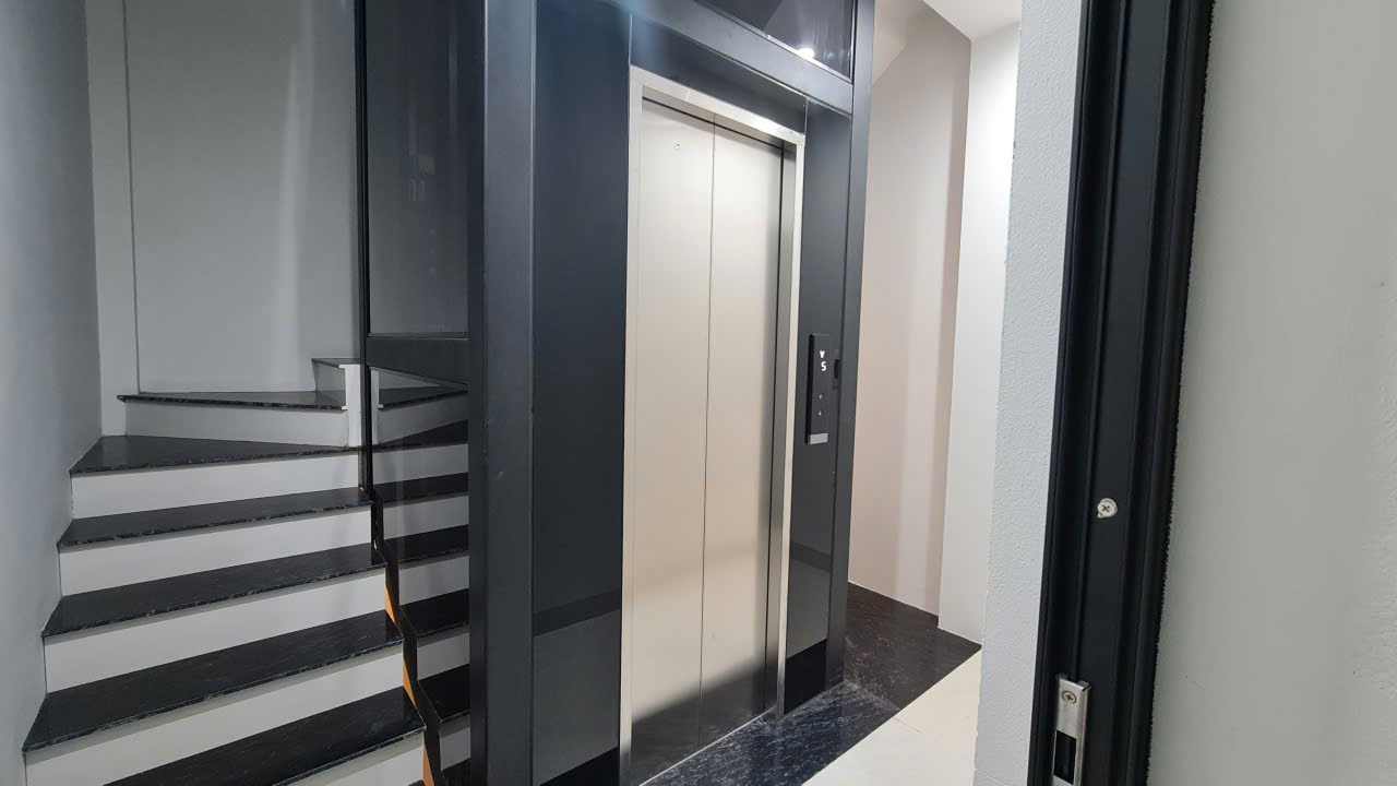 Cửa tầng inox thang máy bên cầu thang lát đá đen trắng, nhà phố 7 tầng tại Hà Đông