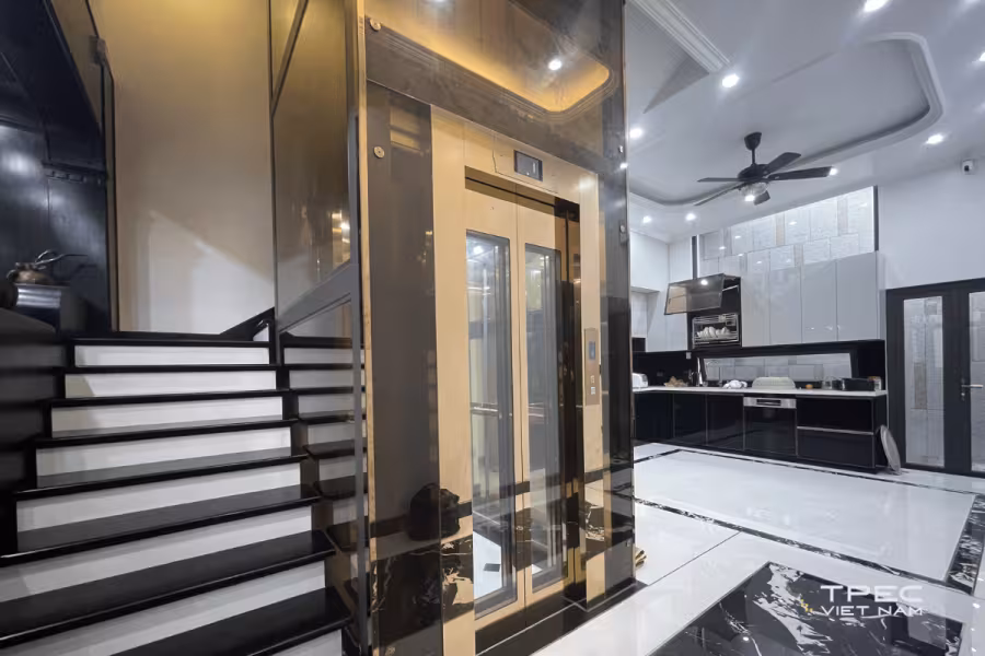Thang máy cáp kéo lắp cạnh cầu thang bộ trong nhà phố, cabin kính khung mạ vàng