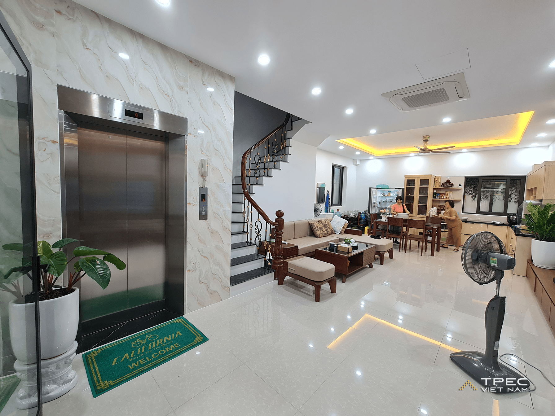 Phòng khách rộng thông bếp có thang máy gia đình và cầu thang gỗ, nhà phố Hoàng Mai