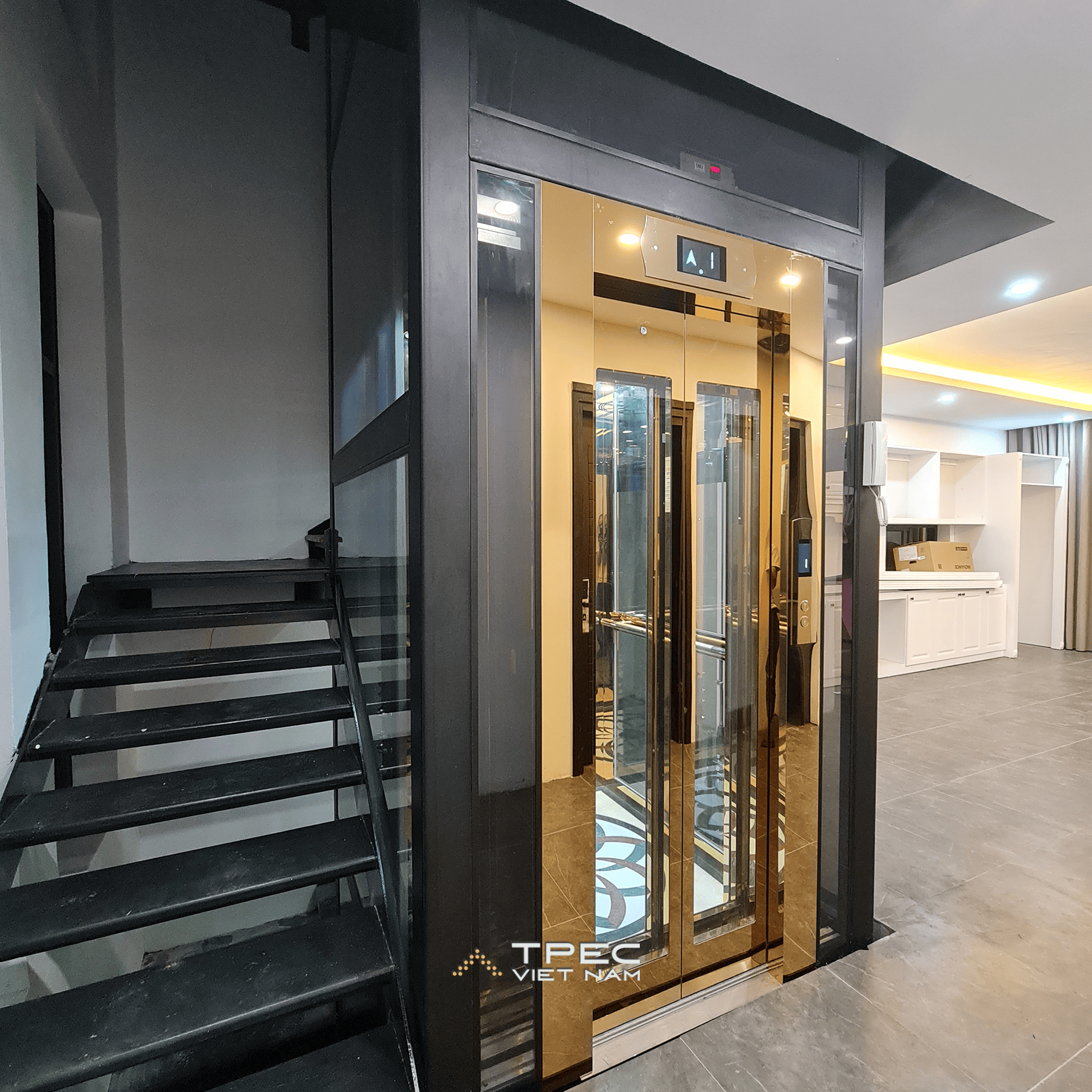 Giếng thang kính khung thép đen và cabin vàng thang máy 630kg bên cầu thang tại Sơn Tây
