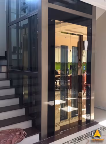 Thang máy gia đình cabin gương đồng, khung nhôm giếng kính đen bên hông cầu thang ốp đá