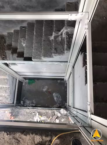 Hố thang lắp khung nhôm thang máy màu ghi bạc bên cạnh cầu thang bê tông, góc nhìn từ trên xuống đáy hố