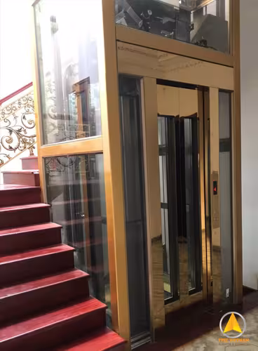 Thang máy khung thép sơn tĩnh điện màu vàng gold, cửa cabin inox gương cạnh cầu thang