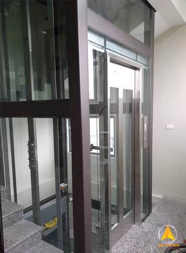 Thang máy khung thép chấn định hình màu nâu, cửa cabin inox lắp trong nhà bên cầu thang