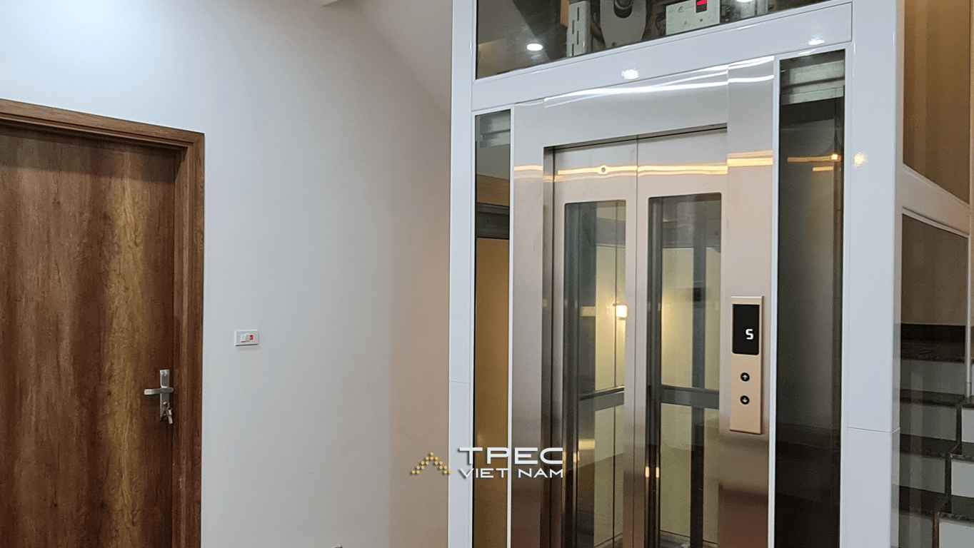 Thang máy kính khung trắng, cửa inox champagne trong sảnh nhà phố Him Lam Vạn Phúc