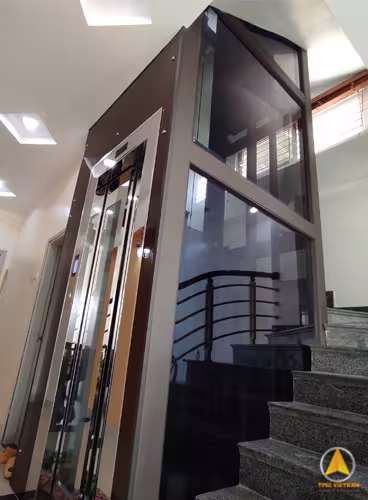 Thang máy khung thép chấn định hình màu nâu cà phê, vách kính lắp bên cầu thang